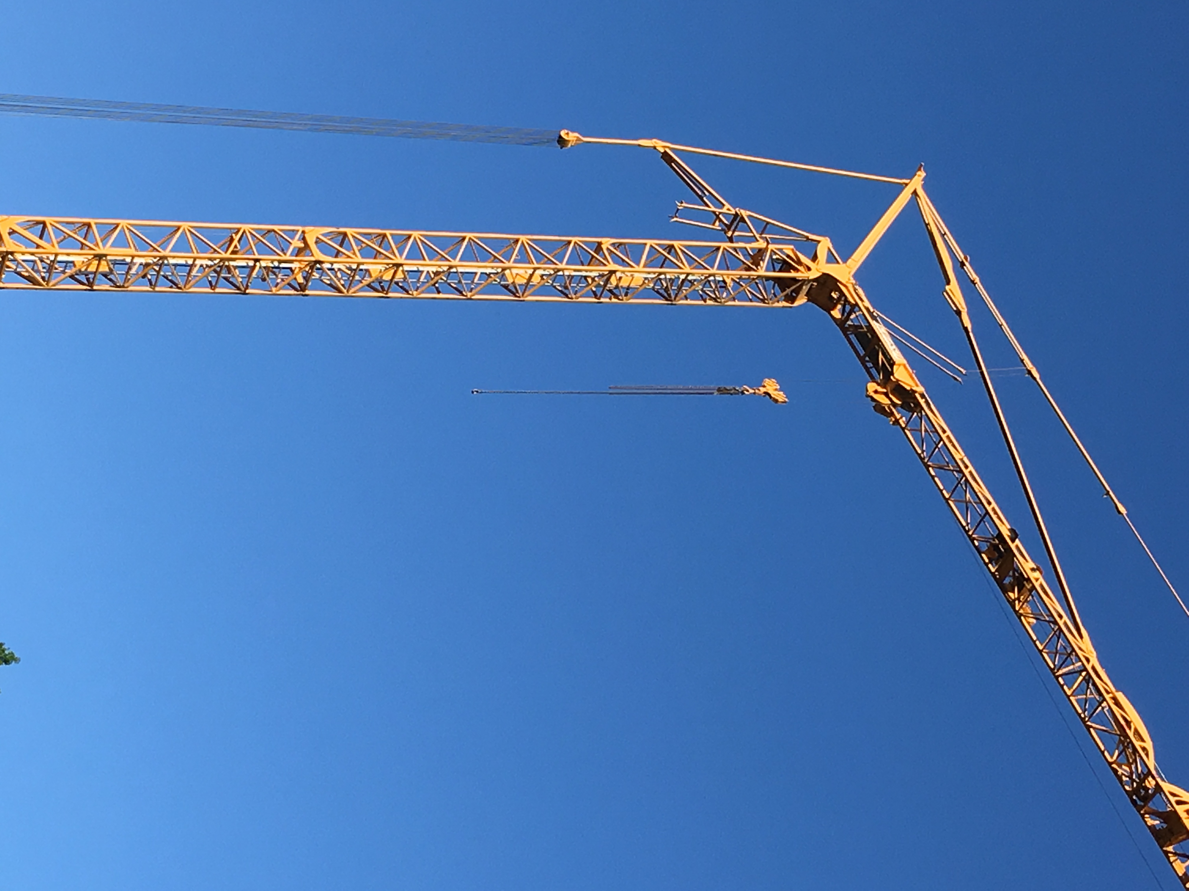 A tall, goldenrod-yellow crane stands above the photo's vantage point, contrasting sharply against a cloudless, bright blue sky.